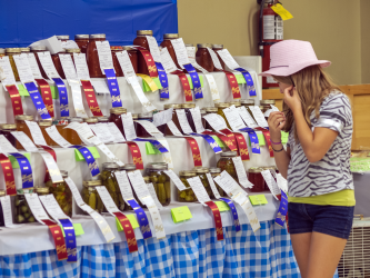 Girl in a pink hat looking at jars with ribbons at a fair display.