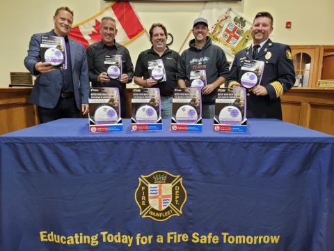 Five men standing behind a table with smoke alarms, promoting fire safety.