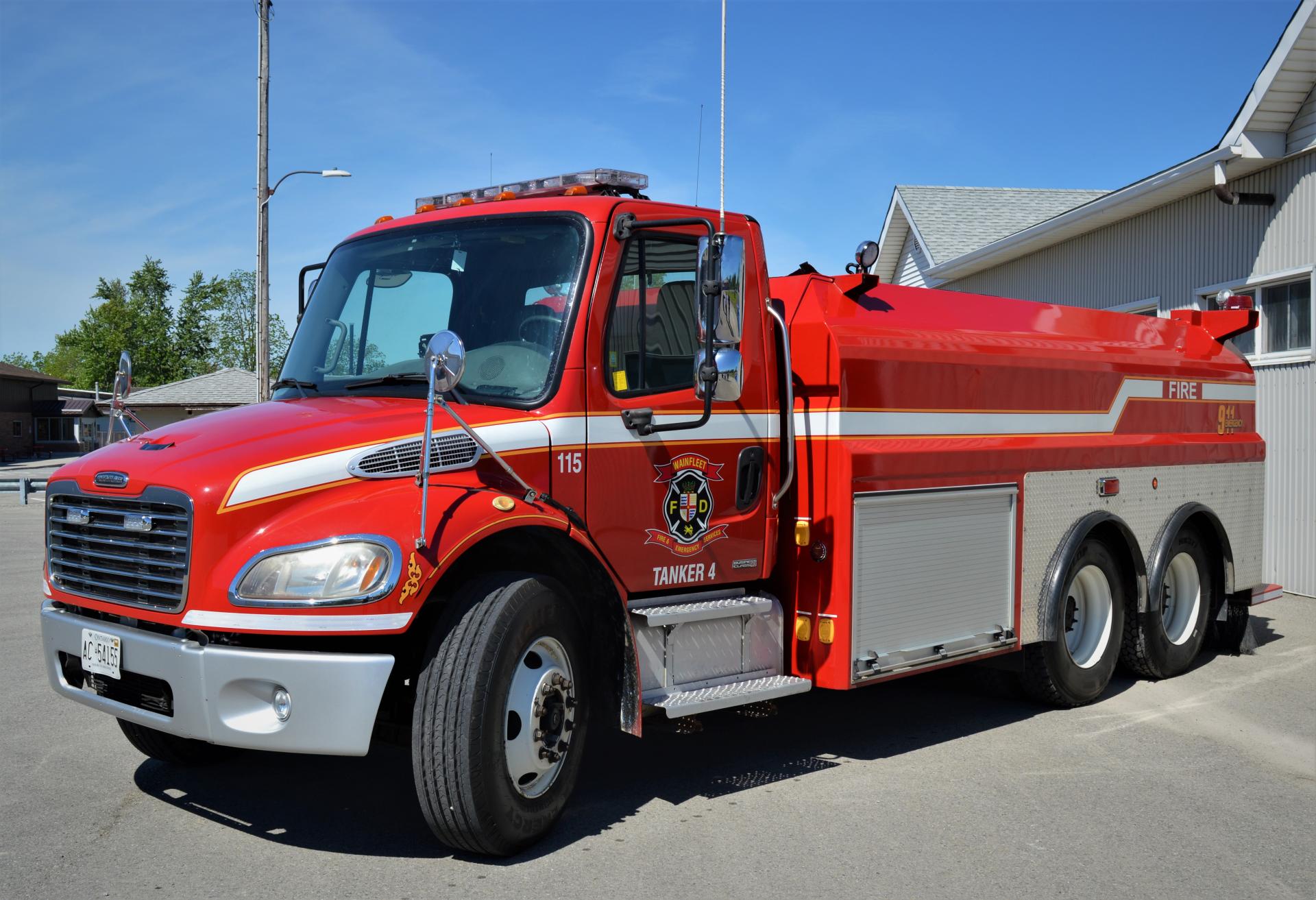 Red fire tanker marked 115 with Wainfleet Fire Department logo, parked outside.